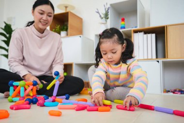 Mutlu bebek kız ve anne evde renkli manyetik inşaat oyuncağı oynuyorlar.