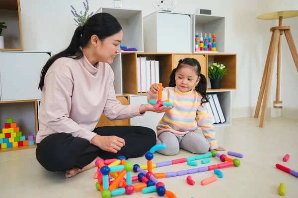 Mutlu bebek kız ve anne evde renkli manyetik inşaat oyuncağı oynuyorlar.