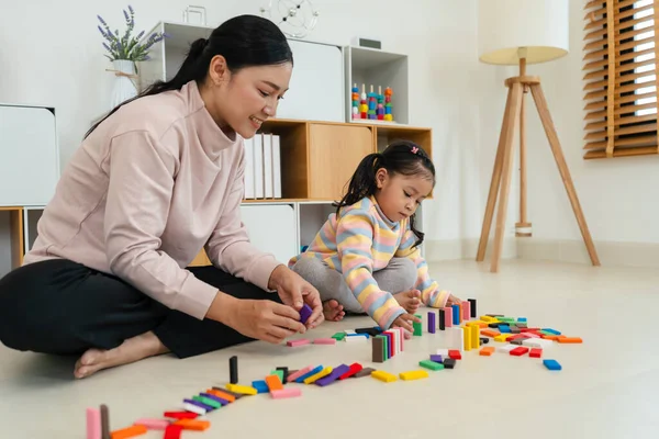 Mutlu küçük kız ve anne renkli tahta blok oyuncağı ya da domino oyunu oynuyorlar.