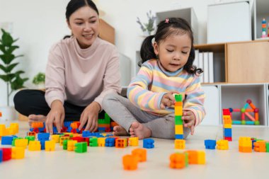 Mutlu küçük kız ve annesi evde oyuncak ya da plastik tuğla oyunu oynuyorlar.