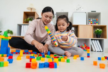 Mutlu küçük kız ve annesi evde oyuncak ya da plastik tuğla oyunu oynuyorlar.