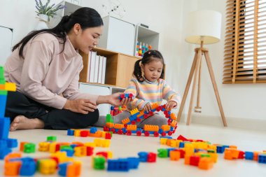 Mutlu küçük kız ve annesi evde oyuncak ya da plastik tuğla oyunu oynuyorlar.