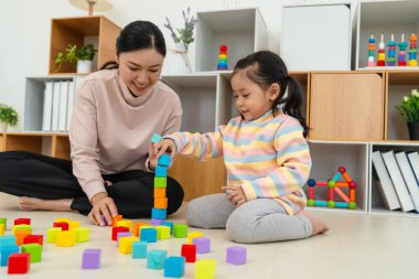 Yeni yürümeye başlayan mutlu kız, annesiyle evde tahta bloklu oyuncak küpler oynuyor.