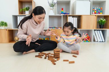 Küçük kız annesiyle birlikte tahta blok oyuncağı oynuyor ve kule çökmesiyle şok oluyor.