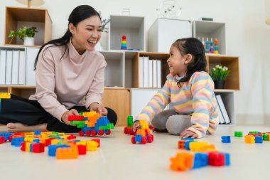 Mutlu küçük kız ve annesi evde oyuncak ya da plastik tuğla oyunu oynuyorlar.