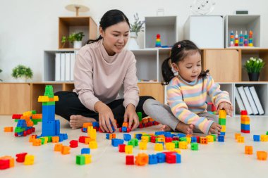 Mutlu küçük kız ve annesi evde oyuncak ya da plastik tuğla oyunu oynuyorlar.