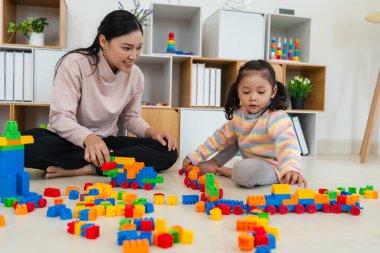 Mutlu küçük kız ve annesi evde oyuncak ya da plastik tuğla oyunu oynuyorlar.