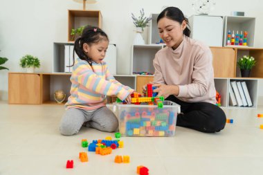 Mutlu küçük kız ve annesi evde oyuncak ya da plastik tuğla oyunu oynuyorlar.