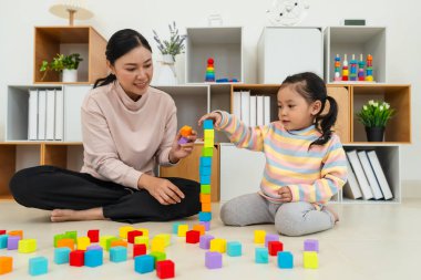 Yeni yürümeye başlayan mutlu kız, annesiyle evde tahta bloklu oyuncak küpler oynuyor.