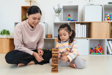 Mutlu küçük kız ve annesi birlikte tahta blok oyuncağı oynuyorlar.