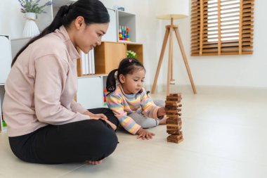 Mutlu küçük kız ve annesi birlikte tahta blok oyuncağı oynuyorlar.