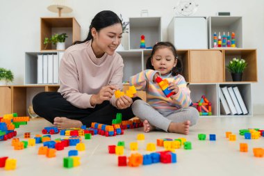 Mutlu küçük kız ve annesi evde oyuncak ya da plastik tuğla oyunu oynuyorlar.