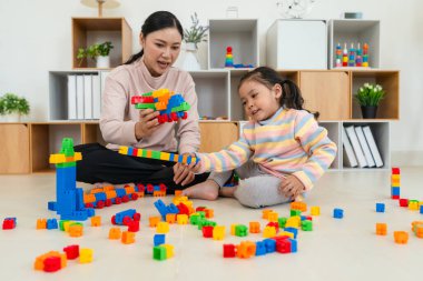 Mutlu küçük kız ve annesi evde oyuncak ya da plastik tuğla oyunu oynuyorlar.