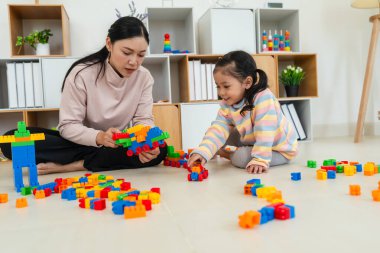 Mutlu küçük kız ve annesi evde oyuncak ya da plastik tuğla oyunu oynuyorlar.