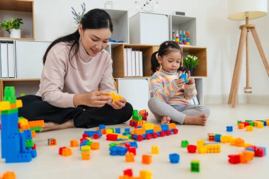Mutlu küçük kız ve annesi evde oyuncak ya da plastik tuğla oyunu oynuyorlar.