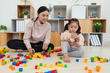 Mutlu küçük kız ve annesi evde oyuncak ya da plastik tuğla oyunu oynuyorlar.