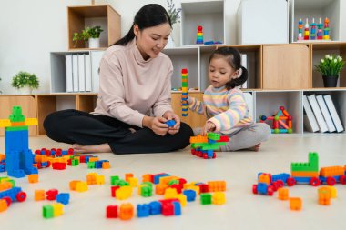 Mutlu küçük kız ve annesi evde oyuncak ya da plastik tuğla oyunu oynuyorlar.