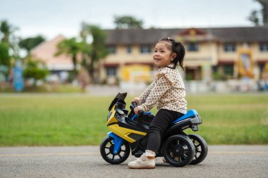 Parkta elektrikli bir motosiklet oyuncağı süren küçük bir kız.