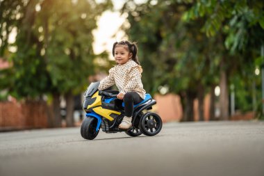 Parkta güneş ışığı olan bir motosiklet oyuncağına binen küçük kız.
