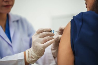 Doktor şırınga tutuyor ve kadın hastaya aşı yapıyor.