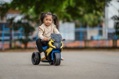 Parkta elektrikli bir motosiklet oyuncağı süren küçük bir kız.