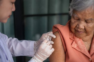 Doktor şırınga tutuyor ve yaşlı kadına aşı yapıyor.