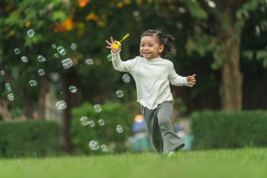 Mutlu küçük kız parkta koşuyor ve sabun köpüğü oynuyor.