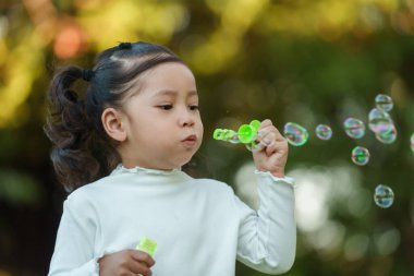 Mutlu küçük kız parkta sabun köpüğü üflüyor.