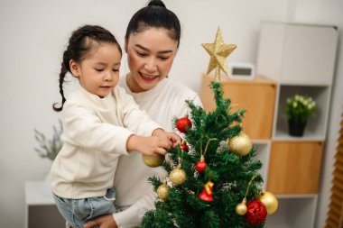 Mutlu anne ve küçük kız Noel ağacını evde oyuncak topla süslüyorlar.