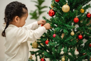 Mutlu küçük kız evde Noel ağacını süslüyor.