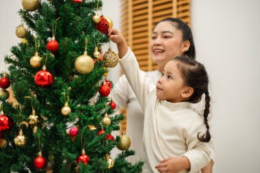 Mutlu anne ve küçük kız Noel ağacını evde oyuncak topla süslüyorlar.
