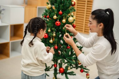 Mutlu anne ve küçük kız evde Noel ağacı süslüyorlar.