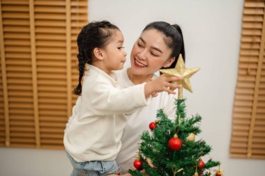 Mutlu anne ve küçük kız evdeki Noel ağacında süsleme yapıyor.