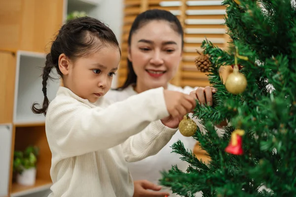 Mutlu anne ve küçük kız Noel ağacını evde oyuncak topla süslüyorlar.