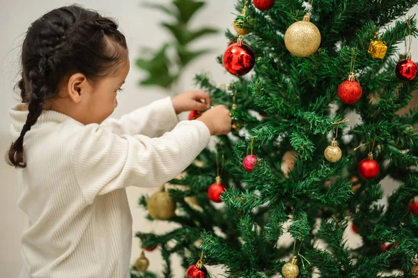 Mutlu küçük kız evde Noel ağacını süslüyor.