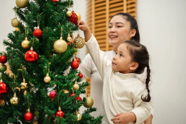 Mutlu anne ve küçük kız Noel ağacını evde oyuncak topla süslüyorlar.