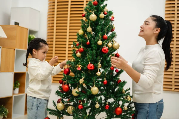 Mutlu anne ve küçük kız evde Noel ağacı süslüyorlar.