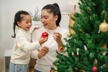 Mutlu anne ve küçük kız Noel ağacını evde oyuncak topla süslüyorlar.