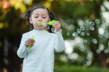 Mutlu küçük kız parkta sabun köpüğü üflüyor.