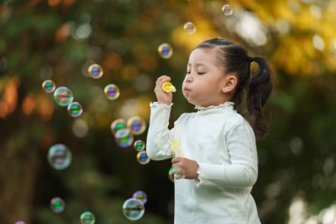 Mutlu küçük kız parkta sabun köpüğü üflüyor.