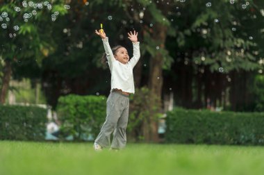 Parkta sabun köpüğü oynayan küçük mutlu kız.