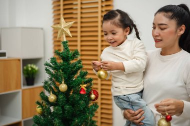 Mutlu anne ve küçük kız Noel ağacını evde oyuncak topla süslüyorlar.