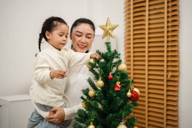 Mutlu anne ve küçük kız Noel ağacını evde oyuncak topla süslüyorlar.