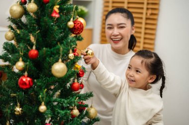 Mutlu anne ve küçük kız Noel ağacını evde oyuncak topla süslüyorlar.