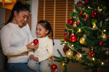 Mutlu anne ve küçük kız gece evde Noel ağacı süslüyorlar.