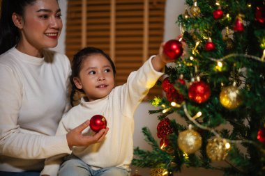 Mutlu anne ve küçük kız gece evde Noel ağacı süslüyorlar.