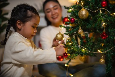 Mutlu anne ve küçük kız gece evde Noel ağacı süslüyorlar.