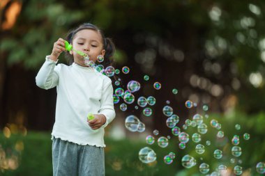 Mutlu küçük kız parkta sabun köpüğü üflüyor.