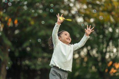 Mutlu küçük kız parkta koşuyor ve sabun köpüğü oynuyor.