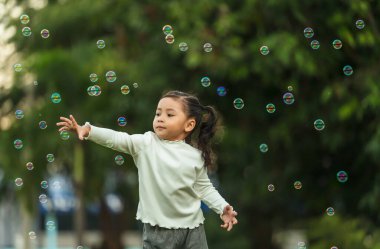 Mutlu küçük kız parkta koşuyor ve sabun köpüğü oynuyor.